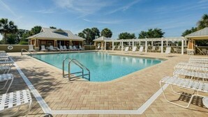 A swimming pool with lounge chairs and umbrellas, surrounded by buildings and palm trees.