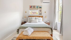 A neatly arranged bedroom with a bed, bedside tables, a woven bench, and framed pictures on the wall. - Rustic Elegance Farmhouse for a tranquil retreat experience in Sanford, FL (Sanford)