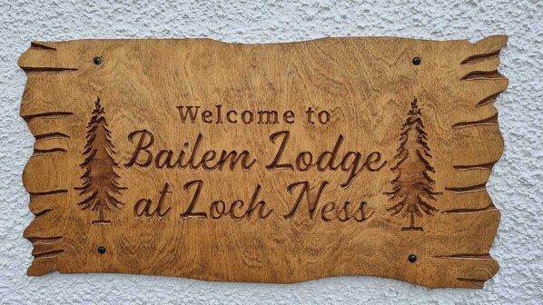 A wooden welcome sign for Bailem Lodge at Loch Ness.