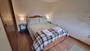 A bedroom with a wooden bed, two bedside lamps, a plaid blanket, and a small rug. - Bailem Lodge at Loch Ness (adults only) (Fort Augustus)