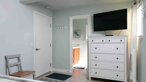 A bedroom with a bed, a dresser, a television, and a door leading to another room.