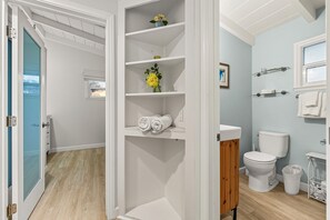 A bathroom with a toilet, sink, and shelves with towels and a vase. - 3BR Combo, Walk To Beach -2 Patios (Ventura)