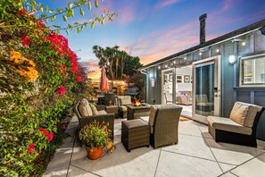 Un espace extérieur aménagé en terrasse, avec des meubles en osier, un foyer et une porte vitrée donnant accès à un espace intérieur.