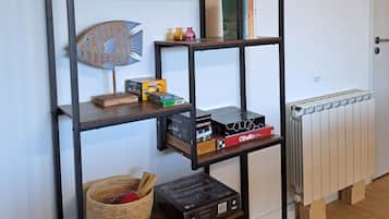 Une pièce avec une étagère en métal noir adossée à un mur blanc, contenant divers objets tels que des jeux de société, une petite plante et des objets décoratifs.