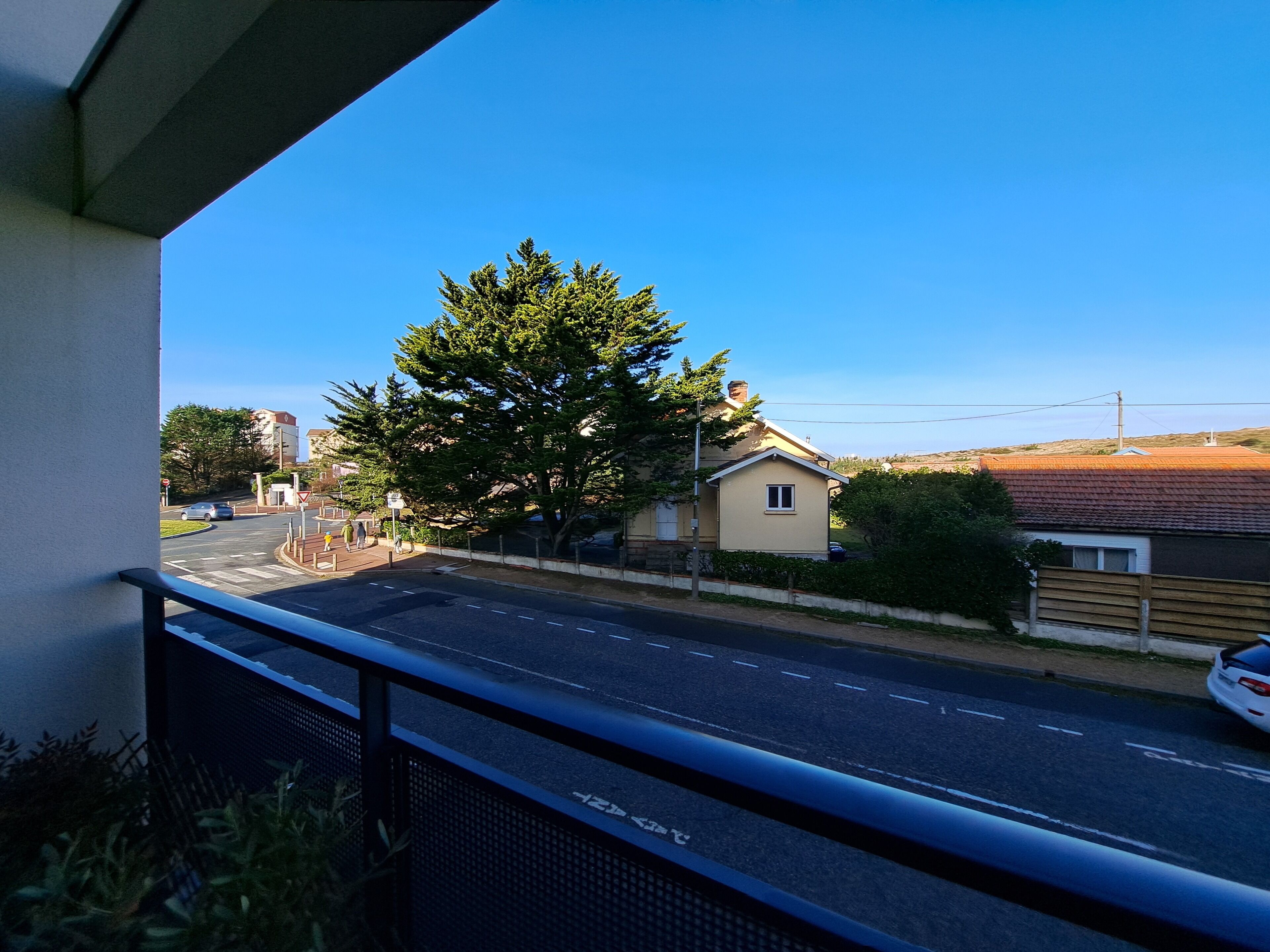 A balcony with a view of a road, a tree, and a building.