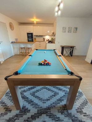 A pool table in a room with a kitchen in the background.