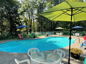 Ein Schwimmbecken mit Liegestühlen und Sonnenschirmen, umgeben von Bäumen.
