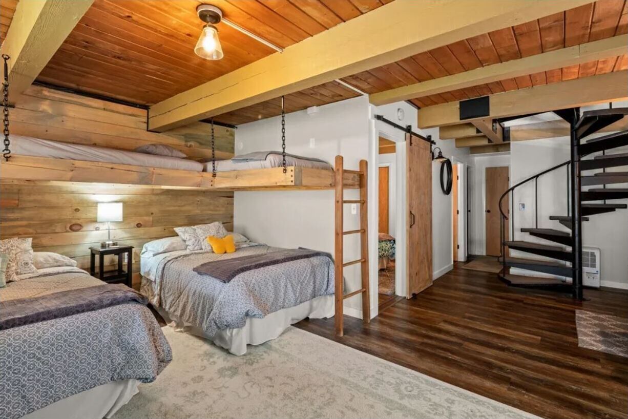 A cozy bedroom with two beds, a wooden ceiling, a ladder, and a spiral staircase.