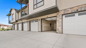 A multi-story residential building with six garage doors, a stone facade, and a balcony with a flower pot. - Northfield Old Town Flat Attached Garage w/ EV (Fort Collins)