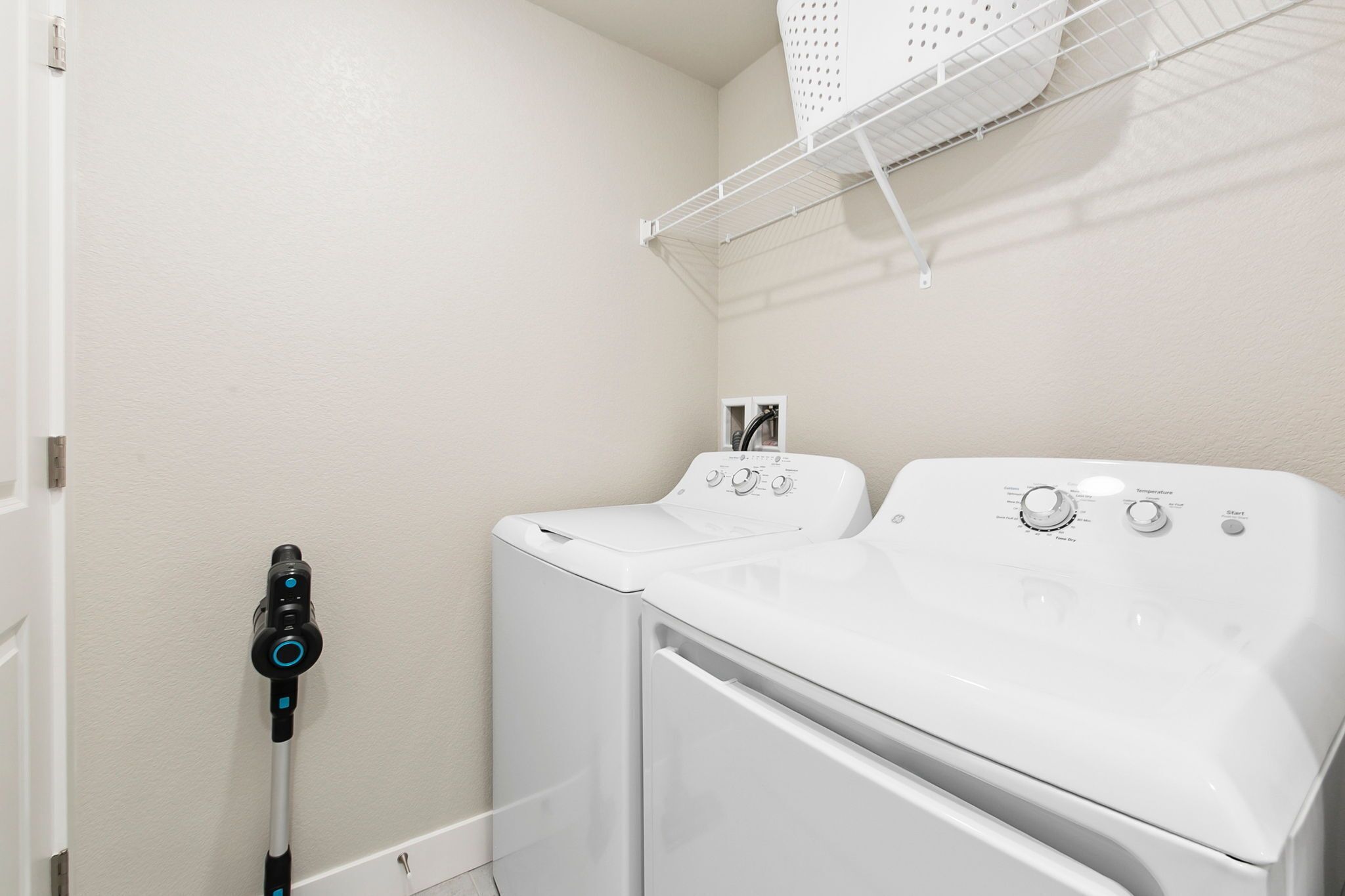 A laundry area with a front-loading washer and dryer, a drying rack, and a wall-mounted laundry basket.