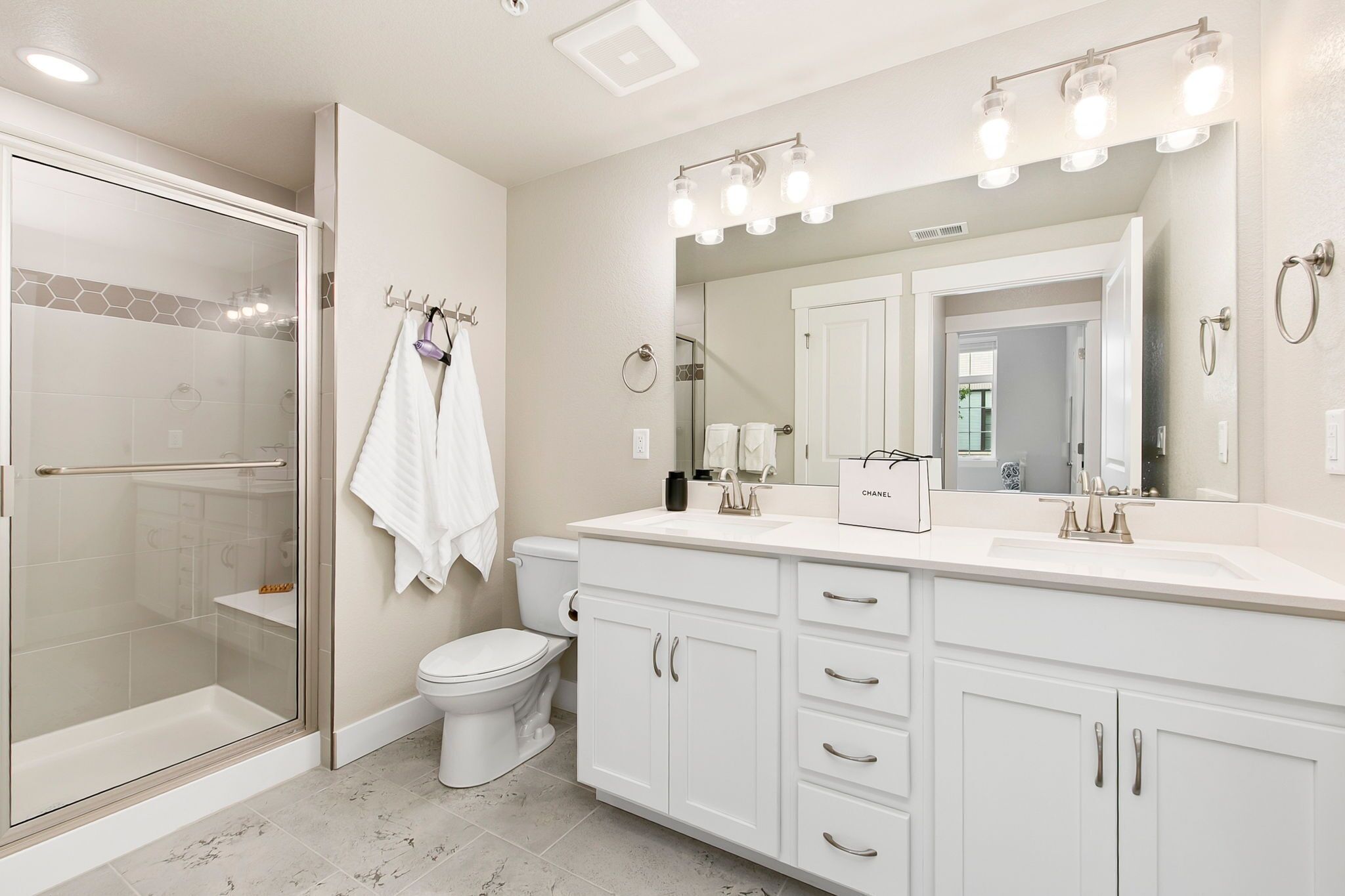 Un bagno moderno con box doccia in vetro, un water, un mobile lavabo con uno specchio grande e una borsa Chanel sul ripiano.
