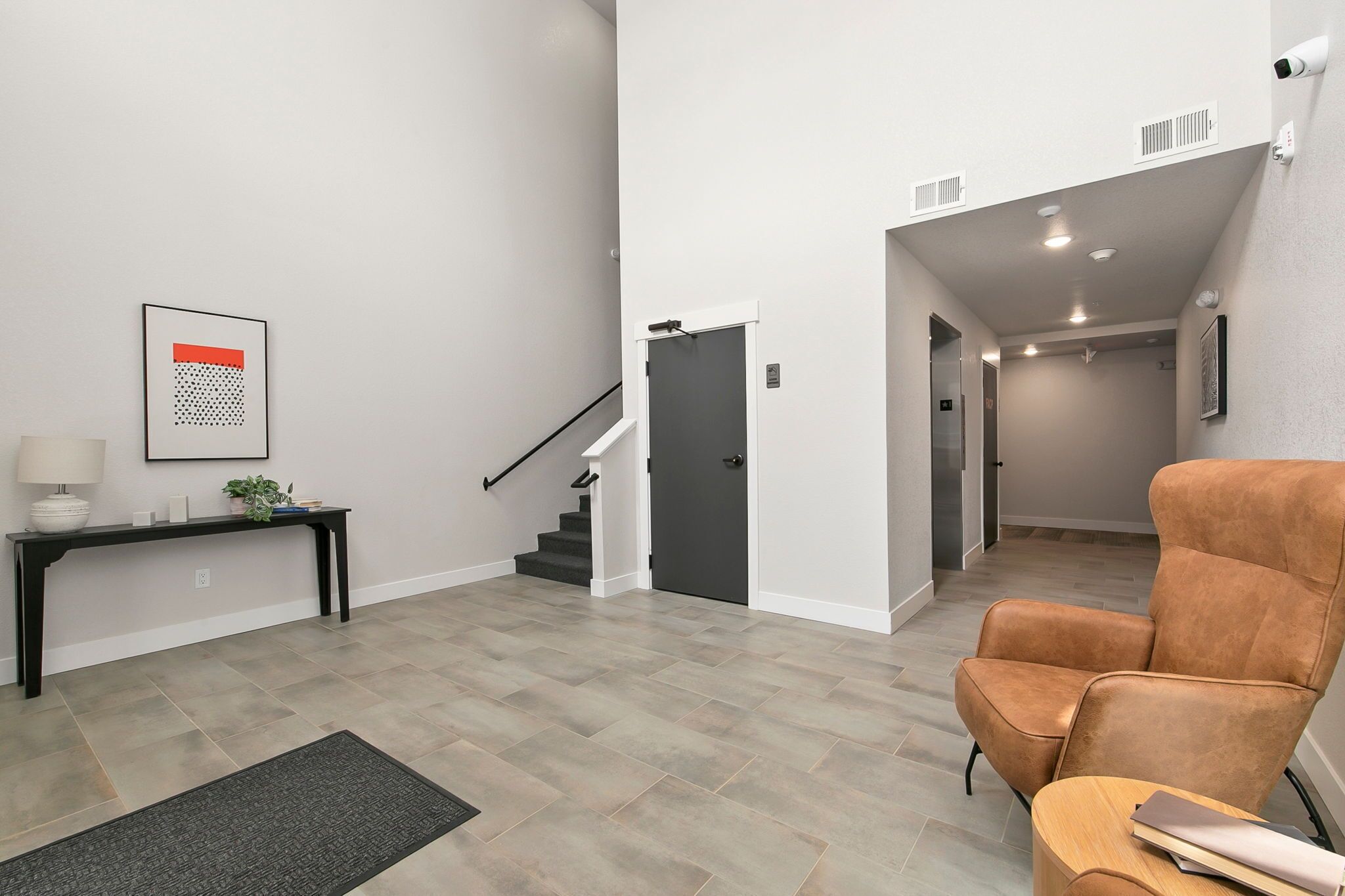 A modern living room with a staircase, a console table with a lamp, and a brown armchair.