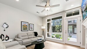 A modern living room with a beige sofa, a black coffee table, a floor lamp, and a large window offering a view of the outside. - Northfield Old Town Flat Attached Garage w/ EV (Fort Collins)