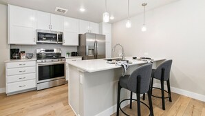 A modern kitchen with white cabinets, stainless steel appliances, and a central island with bar stools. - Northfield Old Town Flat Attached Garage w/ EV (Fort Collins)