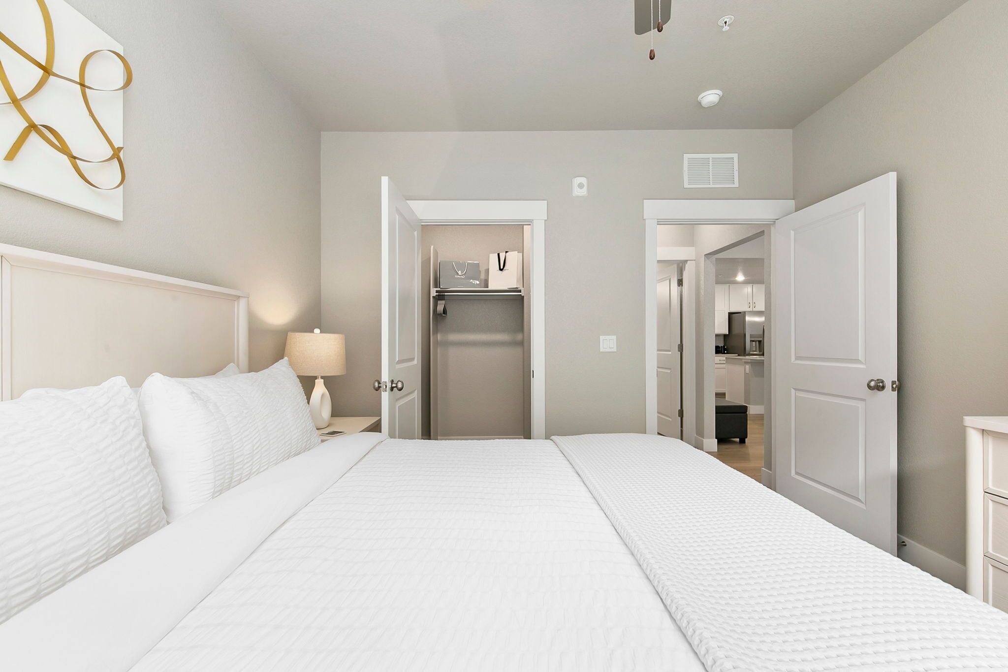 A hotel room with a large bed, a bedside table with a lamp, a wardrobe, and a view into the kitchen area.