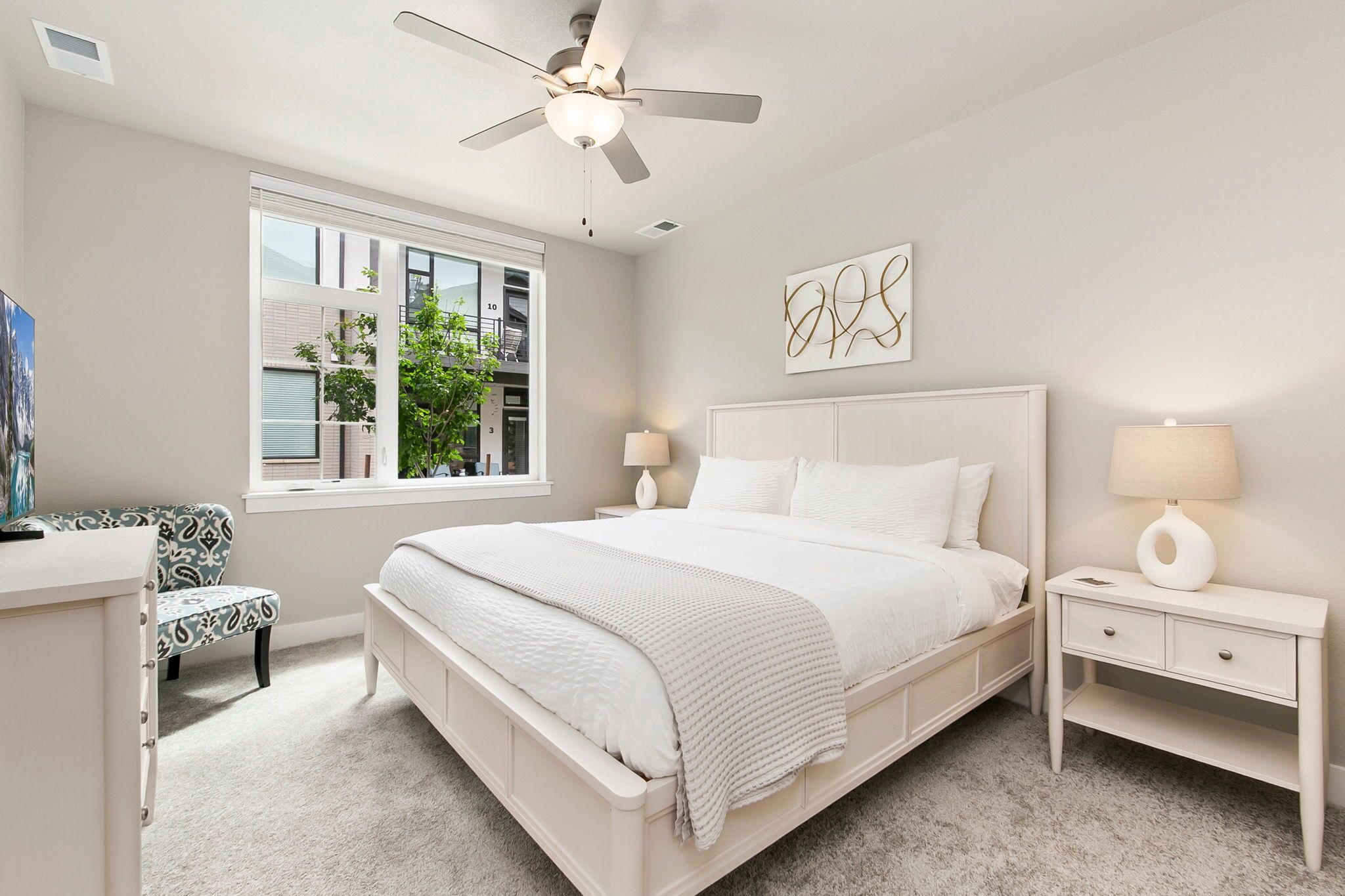 A bedroom with a bed, bedside tables, a chair, a window, and a ceiling fan.