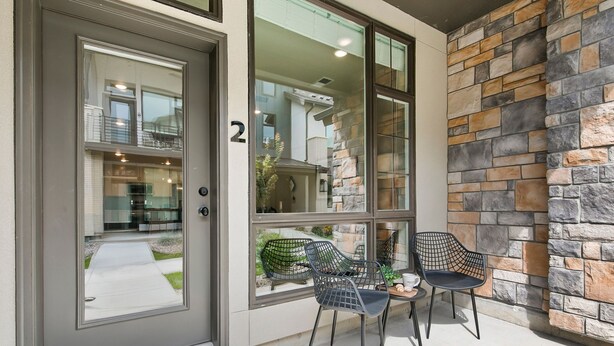 A modern entrance with a glass door, stone wall, and two black chairs outside. - Northfield Old Town Flat Attached Garage w/ EV (Fort Collins)