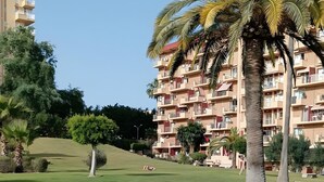 A grassy park area with palm trees and a multi-story building in the background. - Studio 'Benaldream' with Sea View, Shared Pool and Air Conditioning (Benalmádena)