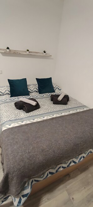 Una cama con una colcha estampada, dos almohadas color turquesa y una toalla enrollada.