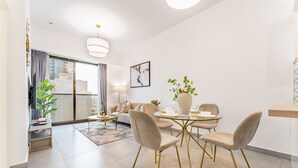 A modern living room with a dining area, featuring a round table with chairs, a sofa, a coffee table, and a potted plant. - Near Circle Mall And Parks, Easy Access to Al Khail Road (Dubai)