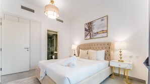 A bedroom with a large bed, a bedside table with a lamp, a wall-mounted artwork, and a door leading to a bathroom. - Near Circle Mall And Parks, Easy Access to Al Khail Road (Dubai)