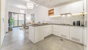A modern kitchen with white cabinets, a herringbone tile backsplash, and a central island with a sink. - Near Circle Mall And Parks, Easy Access to Al Khail Road (Dubai)