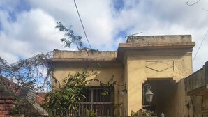Un edificio con fachada color crema, un acceso con puerta de rejas y un pequeño balcón con plantas.