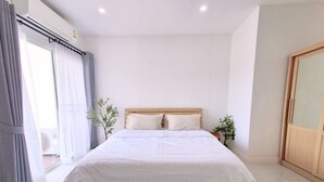 Un dormitorio moderno con una cama grande, cabecera de madera, una planta pequeña y vistas al exterior a través de una ventana.