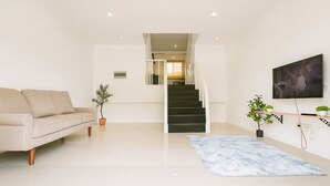 A modern living room with a sofa, a staircase, a TV, and potted plants.