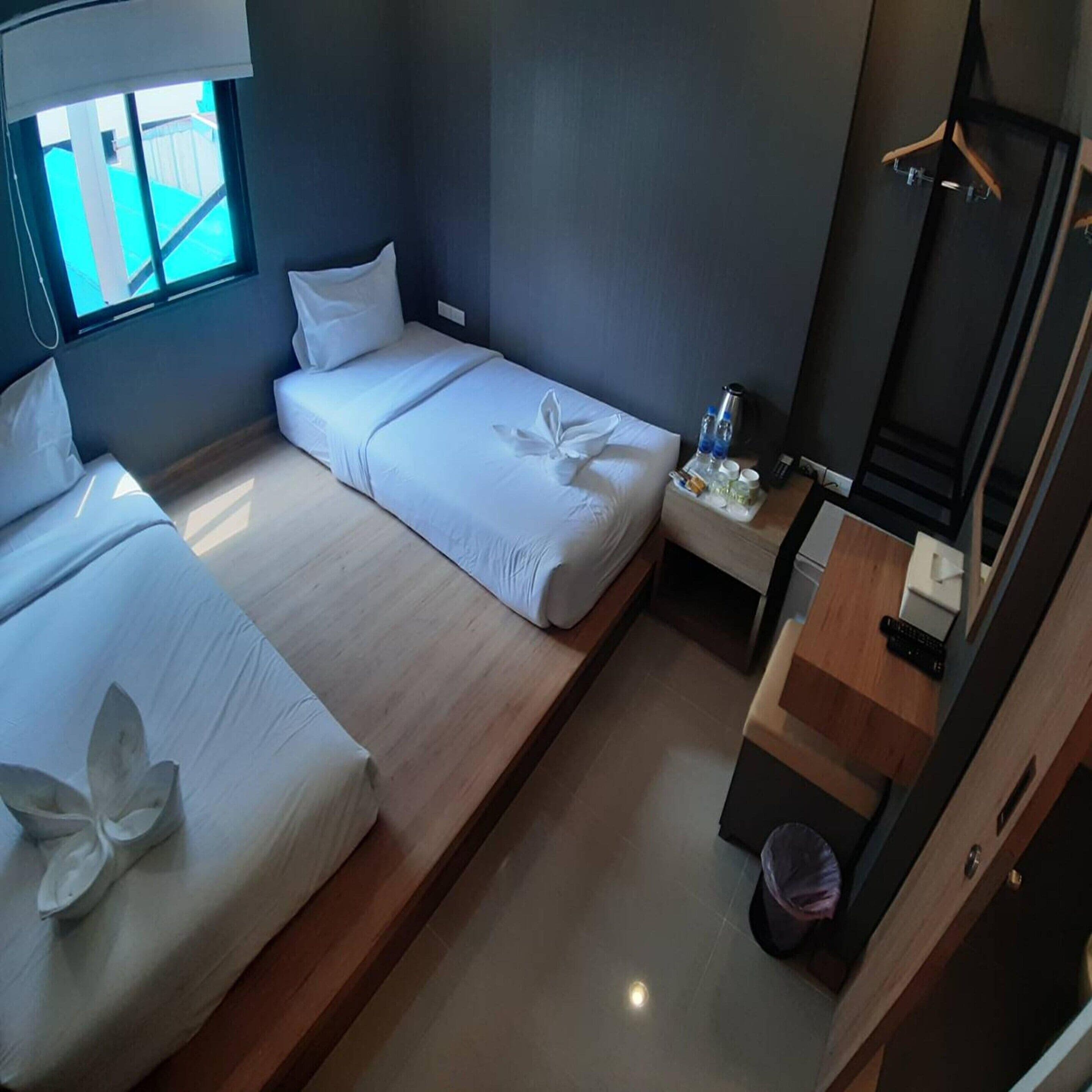 A hotel room with two beds, a small bedside table with a lamp, a mirror, and a window with a view of the outside.
