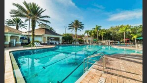 A swimming pool with clear blue water, surrounded by palm trees and lounge chairs.
