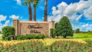 A sign for 'Windor Palms' with a stone facade, palm trees, and a landscaped garden with red and yellow flowers.