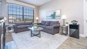 A modern living room with two grey sofas, a glass coffee table, and a large window providing a view of the outdoors.