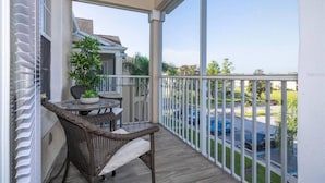 A balcony with wicker furniture, a potted plant, and a view of a parking area and greenery.