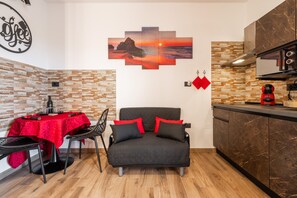 Un espace de vie compact comprenant un coin cuisine, un coin repas avec une nappe rouge et un canapé avec des coussins rouges.