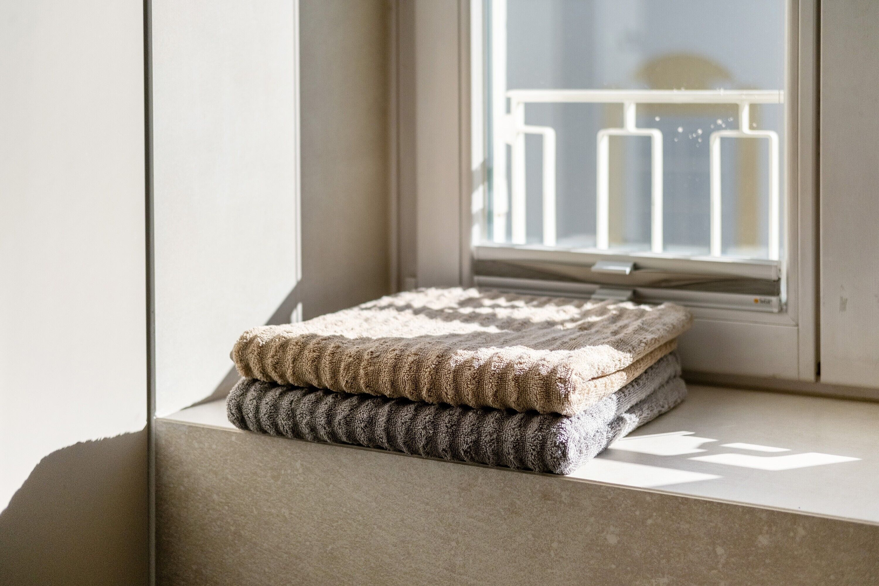 A window with a view of a balcony railing and a window sill with folded blankets.