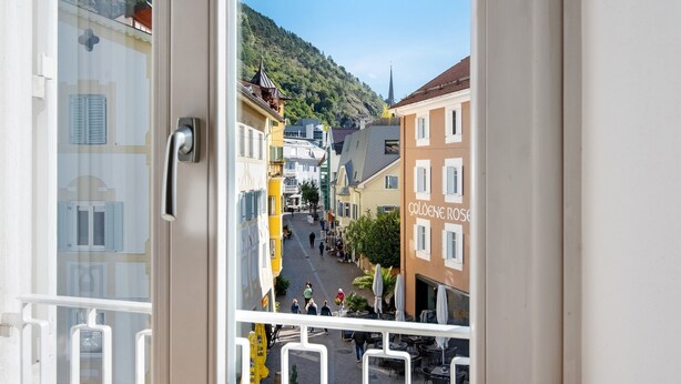 Un balcon donnant sur une rue, des immeubles et une colline.