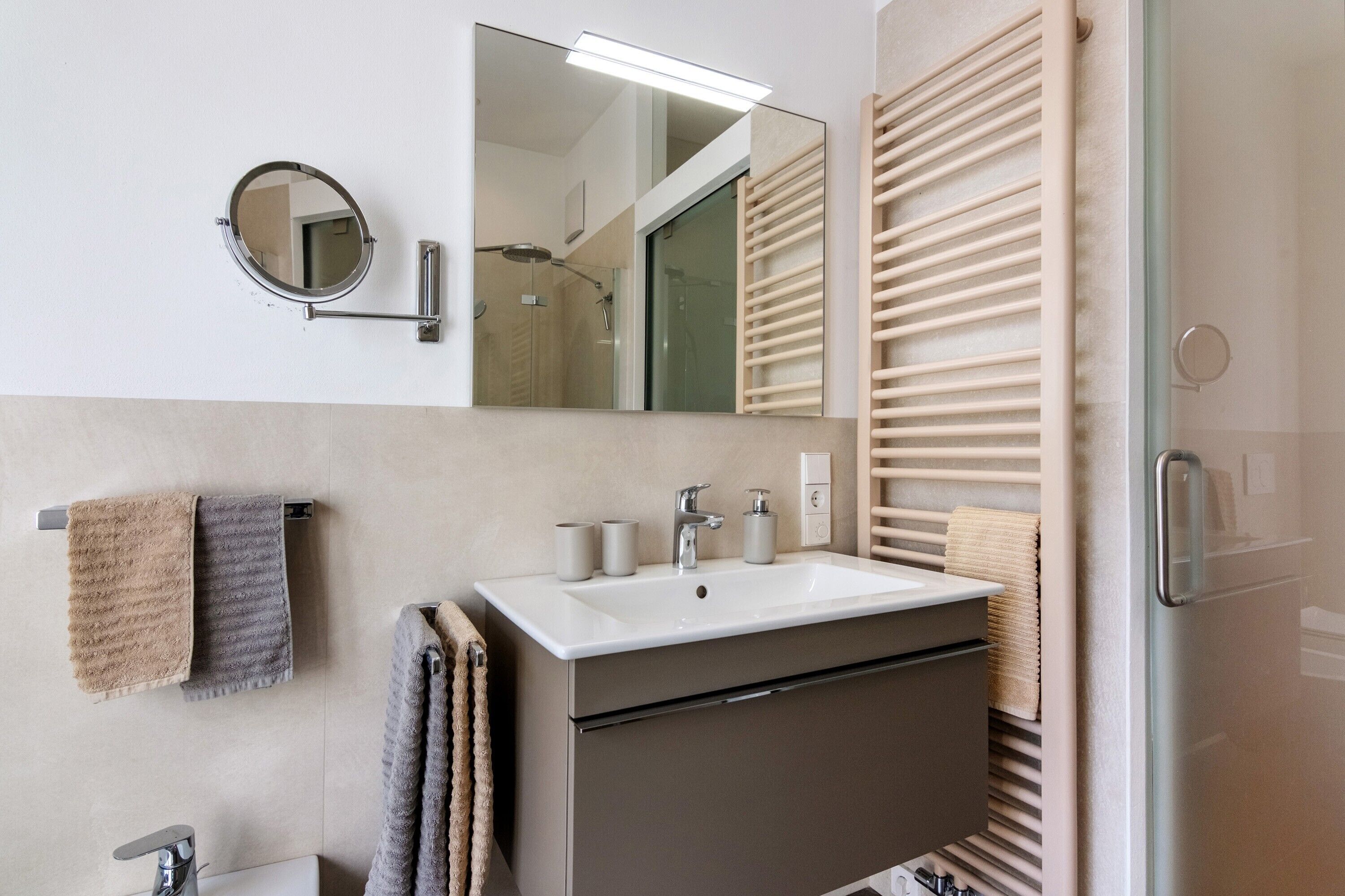 Une salle de bain moderne équipée d’un lavabo, d’un miroir, d’un porte-serviettes et d’une douche à parois de verre.