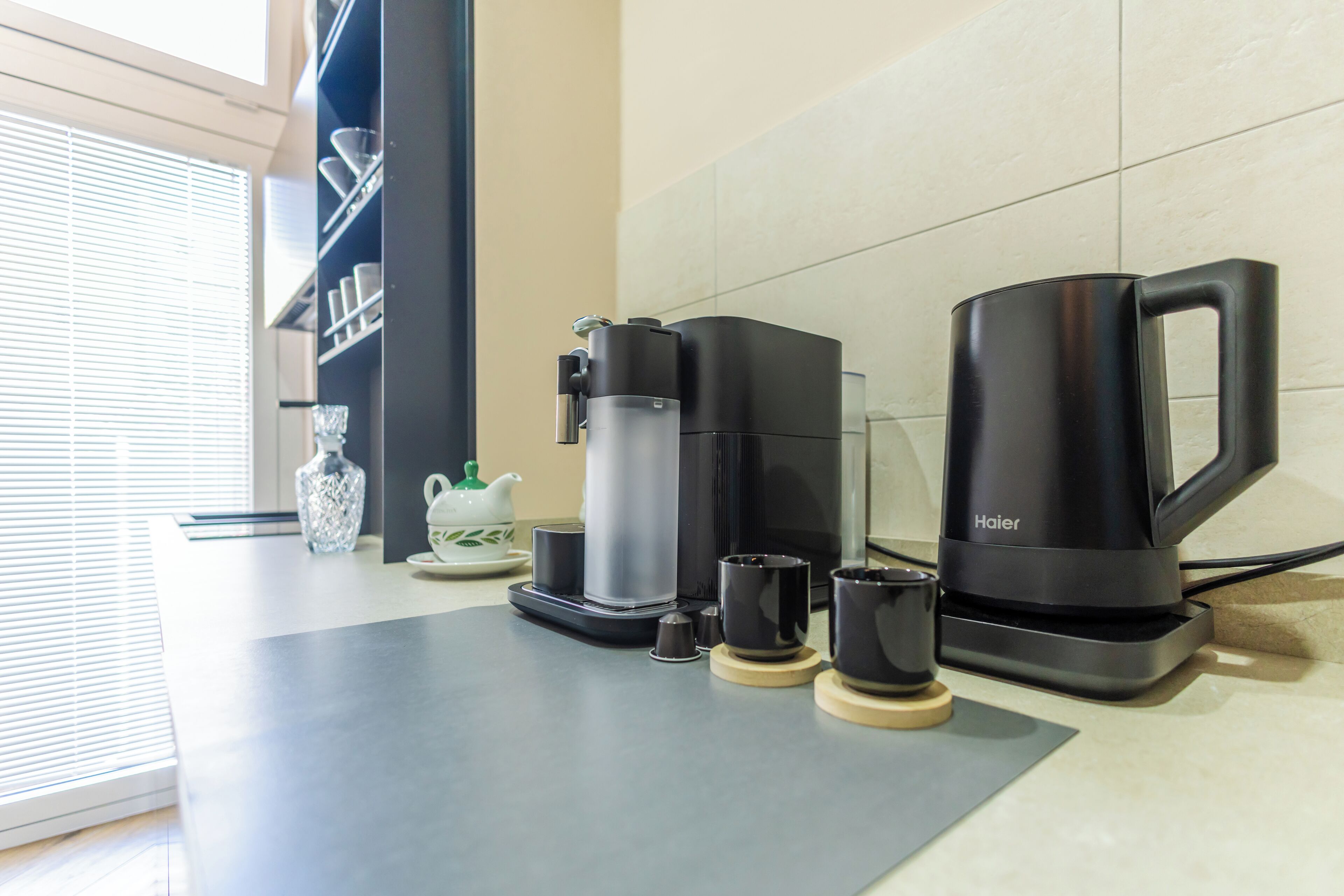 A coffee station with a coffee maker, cups, and a teapot on a countertop.