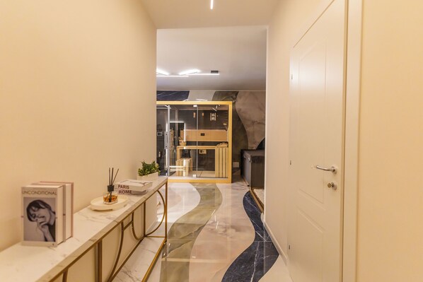 A modern hallway with a marble floor, a white door, and a glass partition leading to a seating area. - VBM SUITE & SPA APARTMENTS (Bari)
