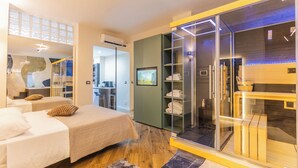 Una habitación de hotel moderna con dos camas, un vestidor amplio con paredes de vidrio y un baño con ducha de vidrio.