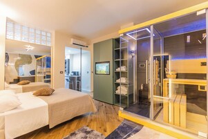 Una moderna camera d'albergo con due letti, un cabina armadio in vetro e un bagno con doccia a vetro.