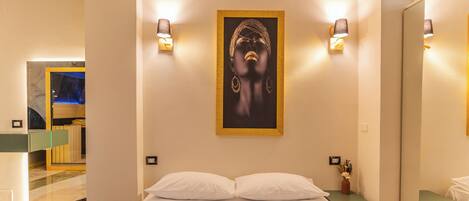 A hotel room with a bed, pillows, a framed artwork, bedside lamps, a mirror, and a small table with a vase.
