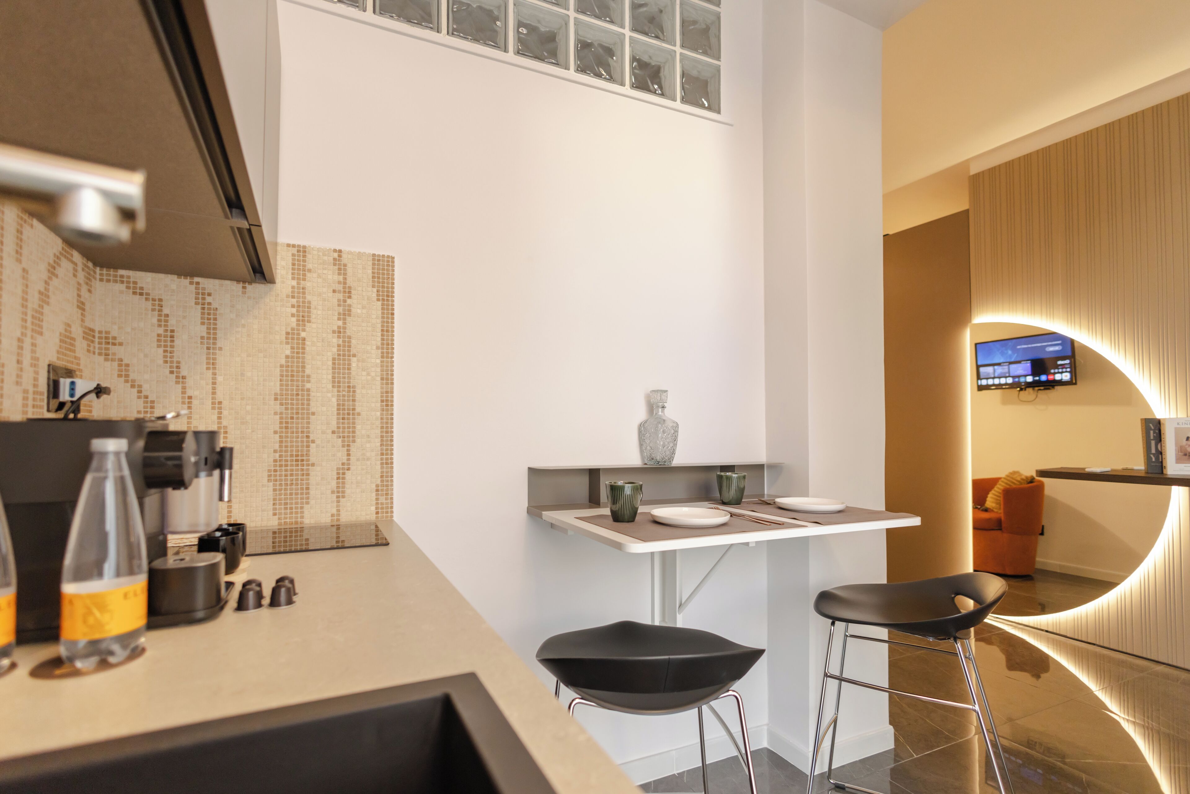 Una cocina moderna con un pequeño comedor, una cafetera y un televisor montado en la pared.