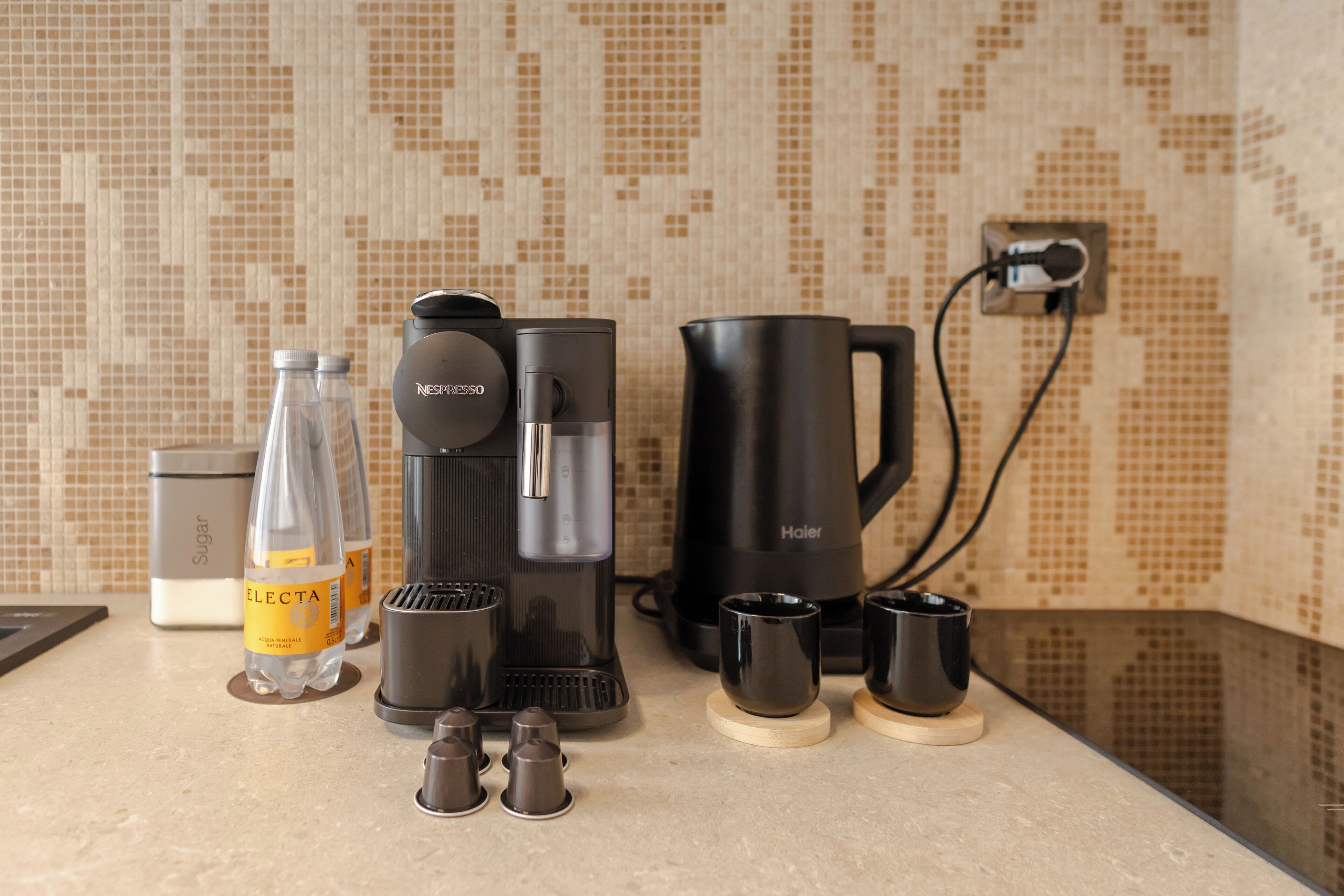 Una encimera de cocina con una cafetera, un dispensador de azúcar y dos botellas de agua.