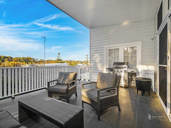 A covered patio with wicker furniture, a grill, and a view of the surrounding landscape.