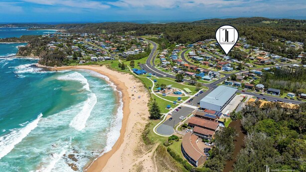 Vista aérea de uma área residencial costeira, com uma praia, casas e um edifício grande com telhado plano.