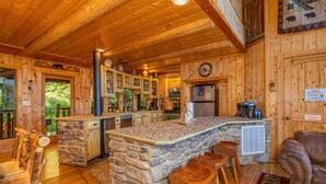 Interior rústico de una cabaña con una barra tipo isla de piedra, muebles de madera y un rincón de estar acogedor.