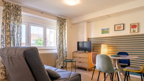 Ein modernes Zimmer mit einer Couch, einem Fernseher, einem kleinen Tisch mit Stühlen und Kunstwerken an der Wand.