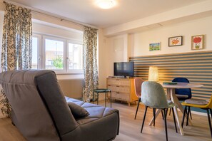 Une chambre moderne avec un canapé, un téléviseur, une petite table avec des chaises et des œuvres d’art au mur.